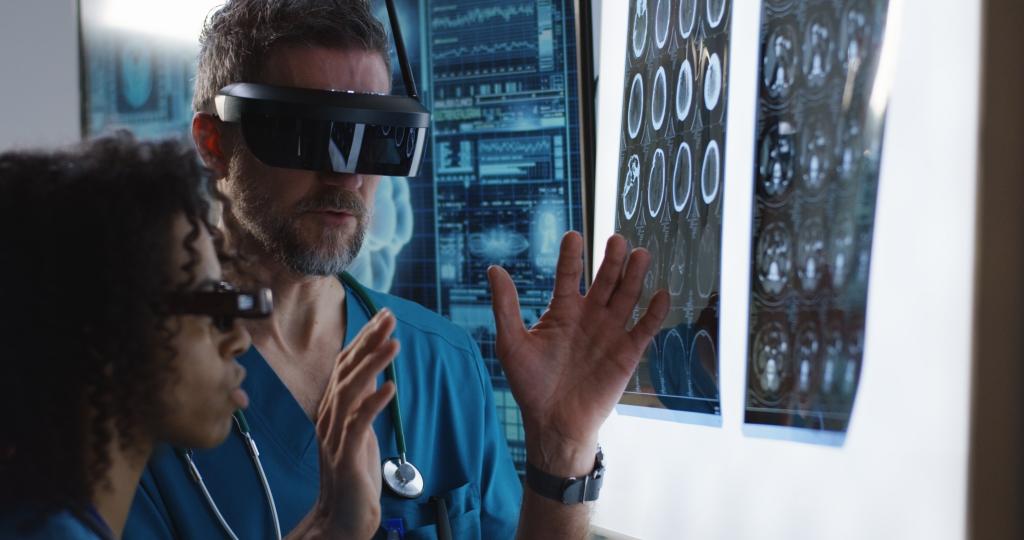 Bilde av to personer med VR-briller på, som står foran en skjerm og gestikulerer og prater.